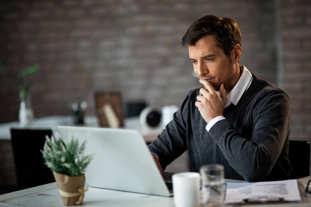 man thinking and using a laptop - How Much Does Speechify Cost